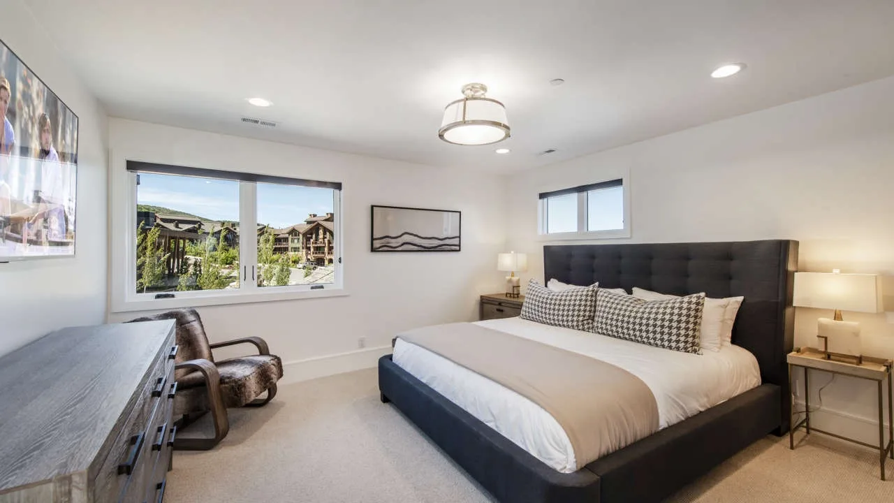 A bedroom with a large bed, dark headboard, and seating beside the window.