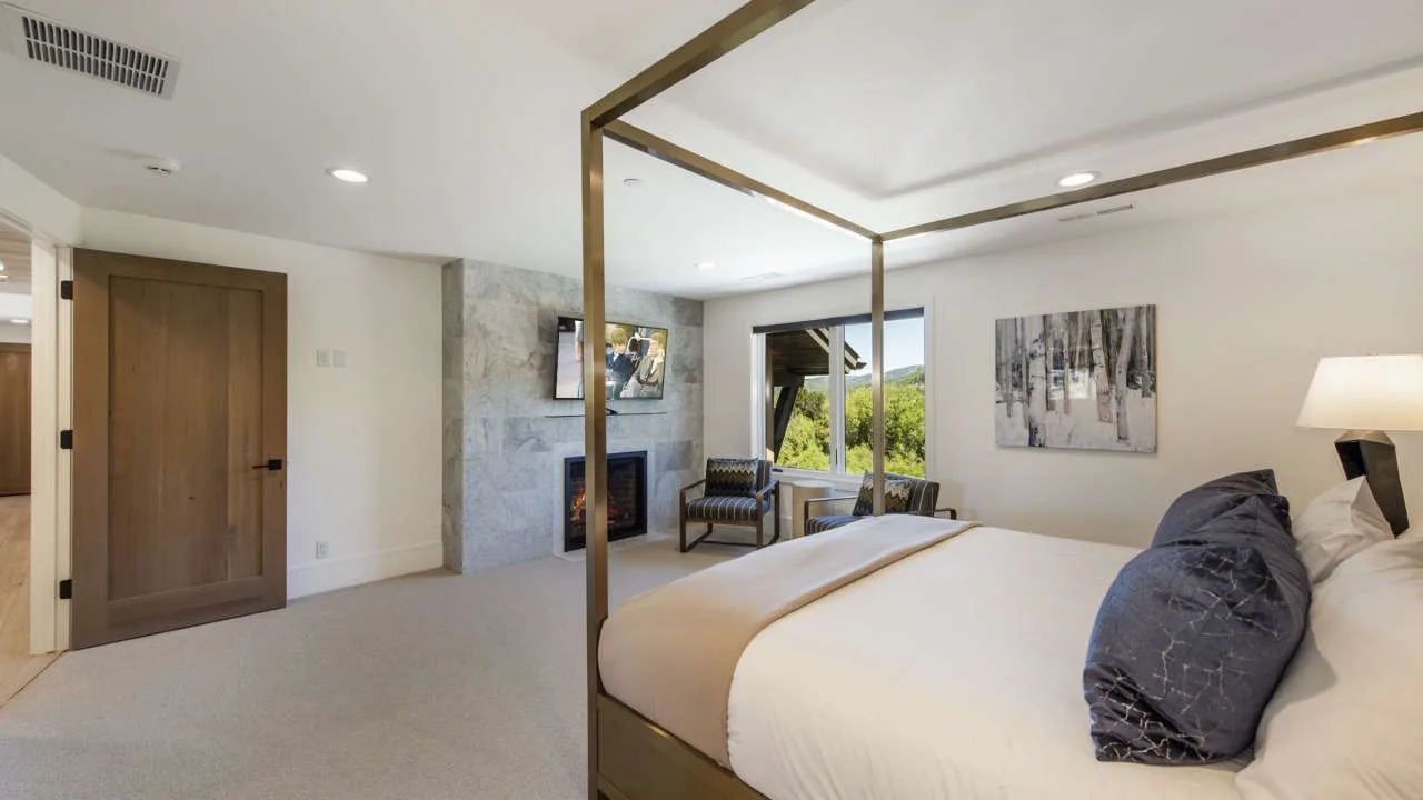 A bedroom with a large bed, a wooden door, and a fireplace.