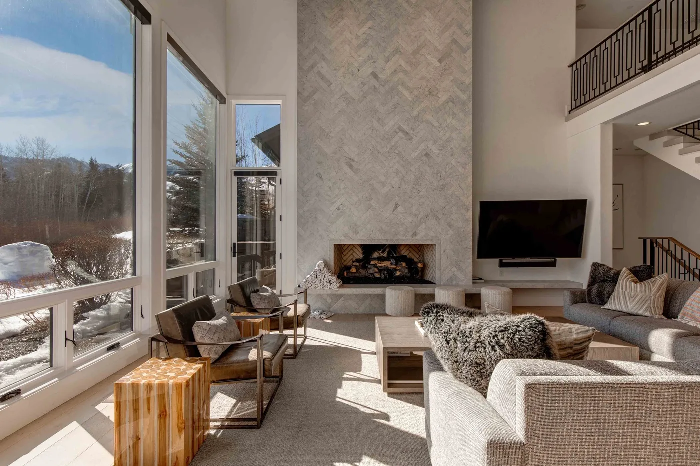 A bright living room with tall windows, seating, and a fireplace.