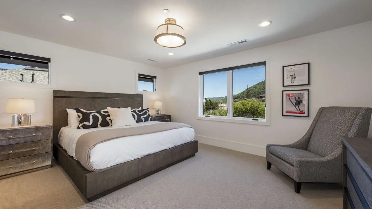 A bedroom with a large bed, a window, and an upholstered chair.