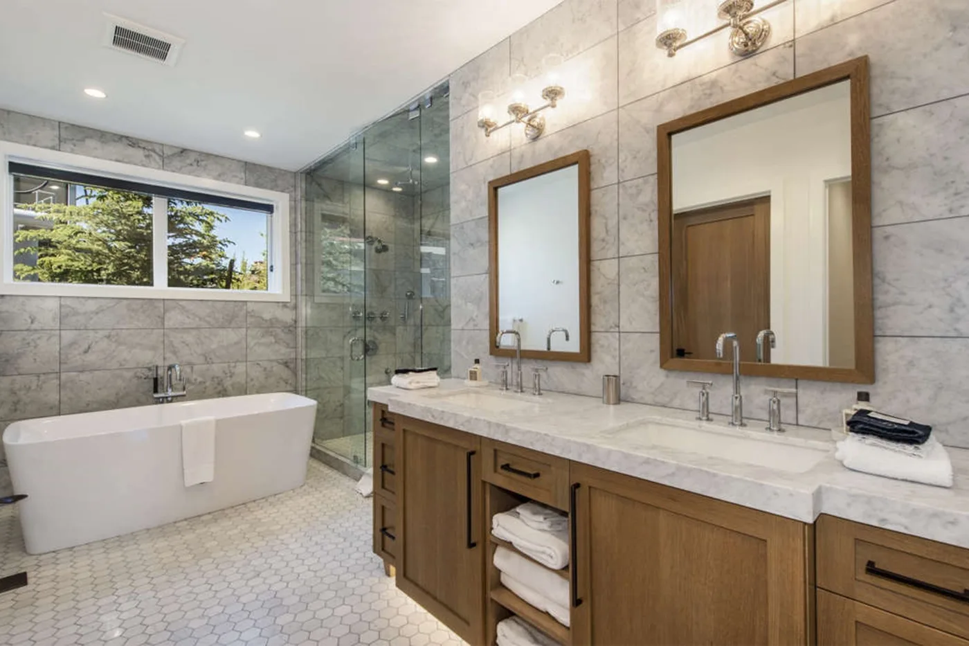 A bright bathroom with a bathtub, glass shower, and double vanity.