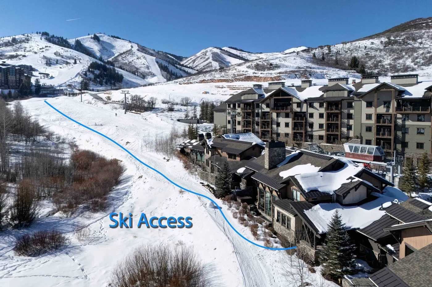 Snow-covered ski slopes wind past a cluster of buildings beneath a clear blue sky.