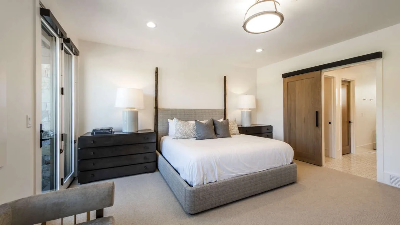 A bright bedroom with a bed, bedside tables, and a sliding glass door.