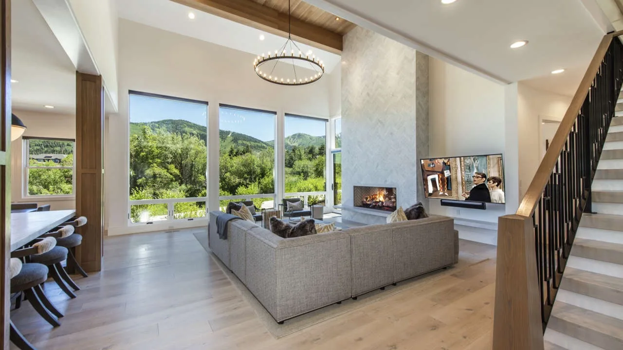 A bright living room with large windows, seating, and a fireplace.