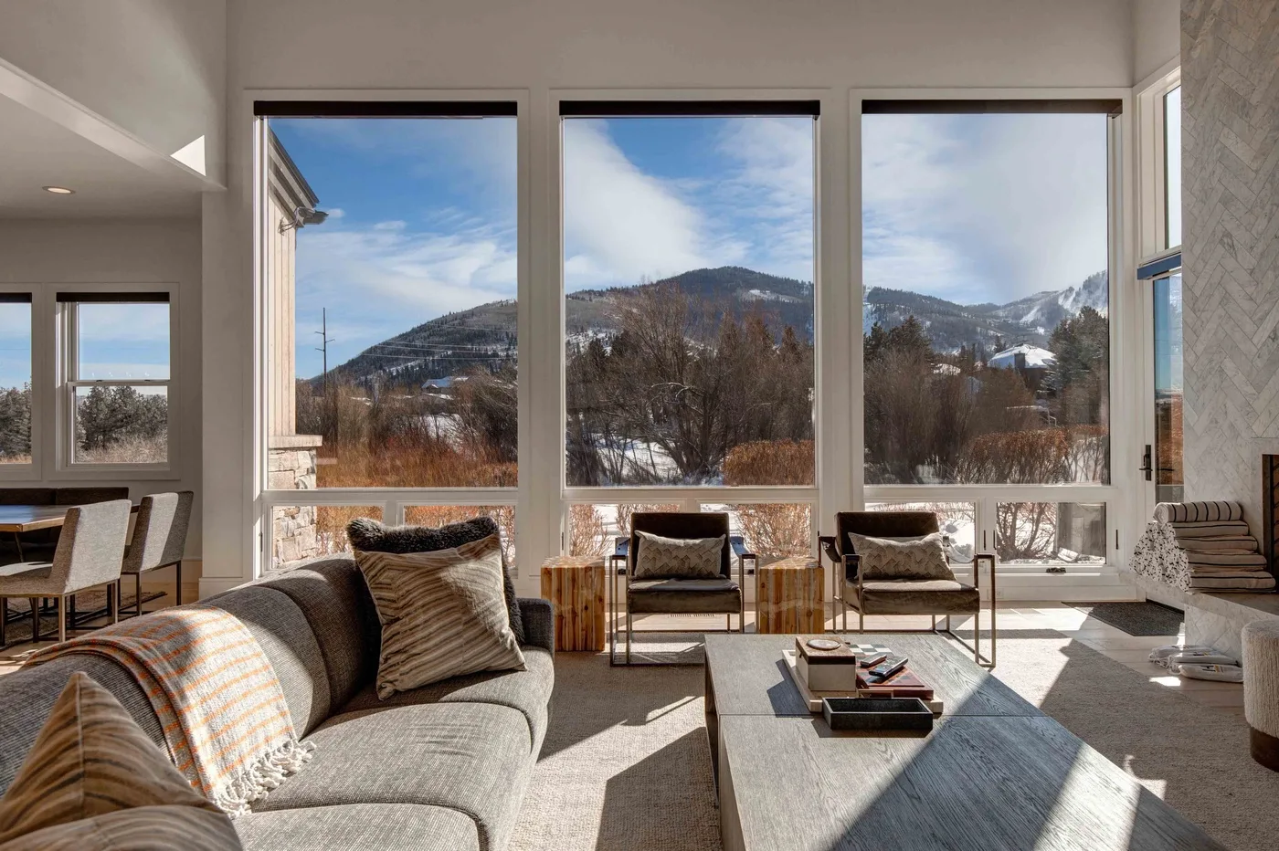 A bright living room with large windows overlooking a snowy mountain landscape.