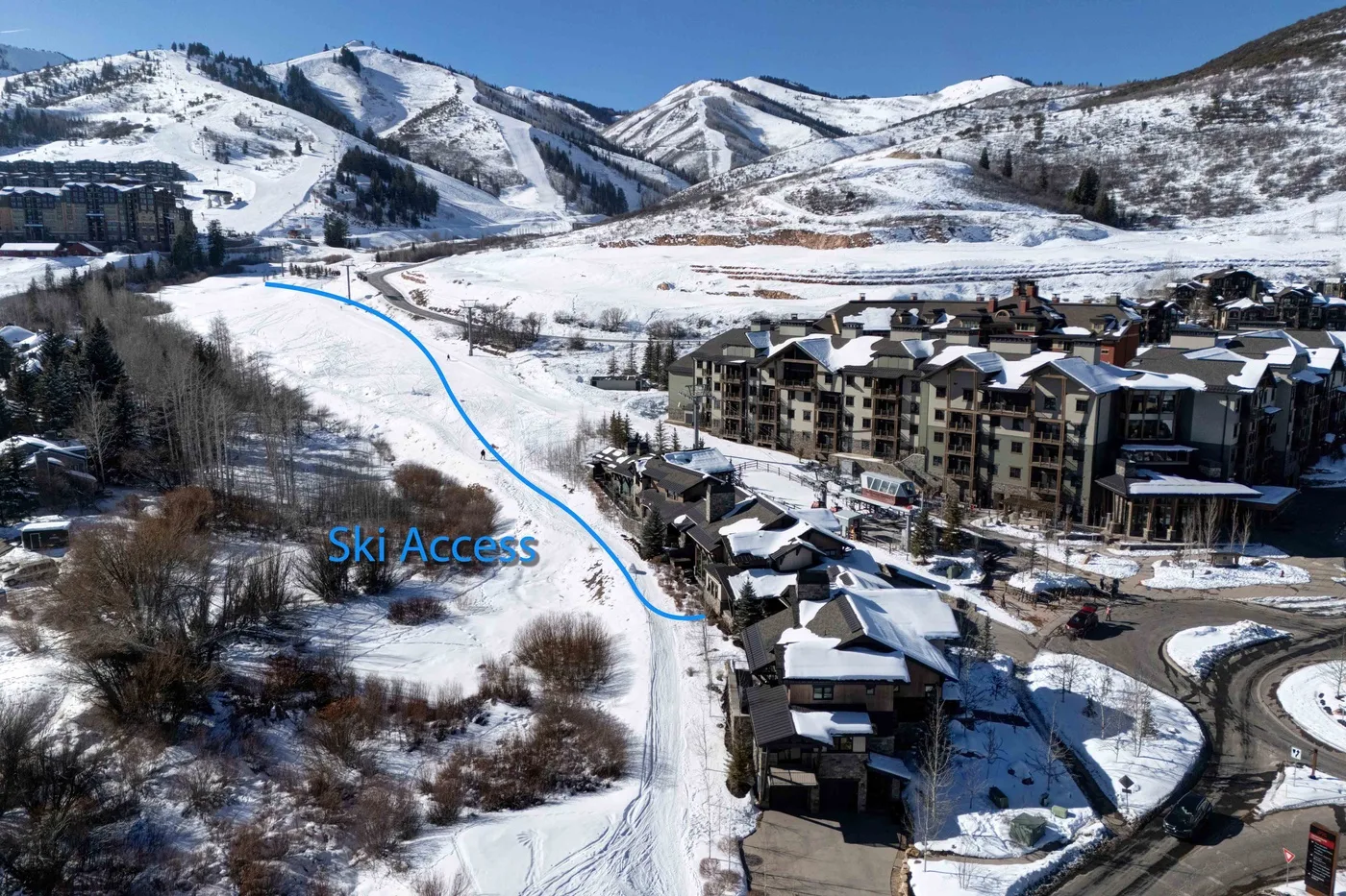 A snowy mountain resort sits beside ski slopes under a clear blue sky.