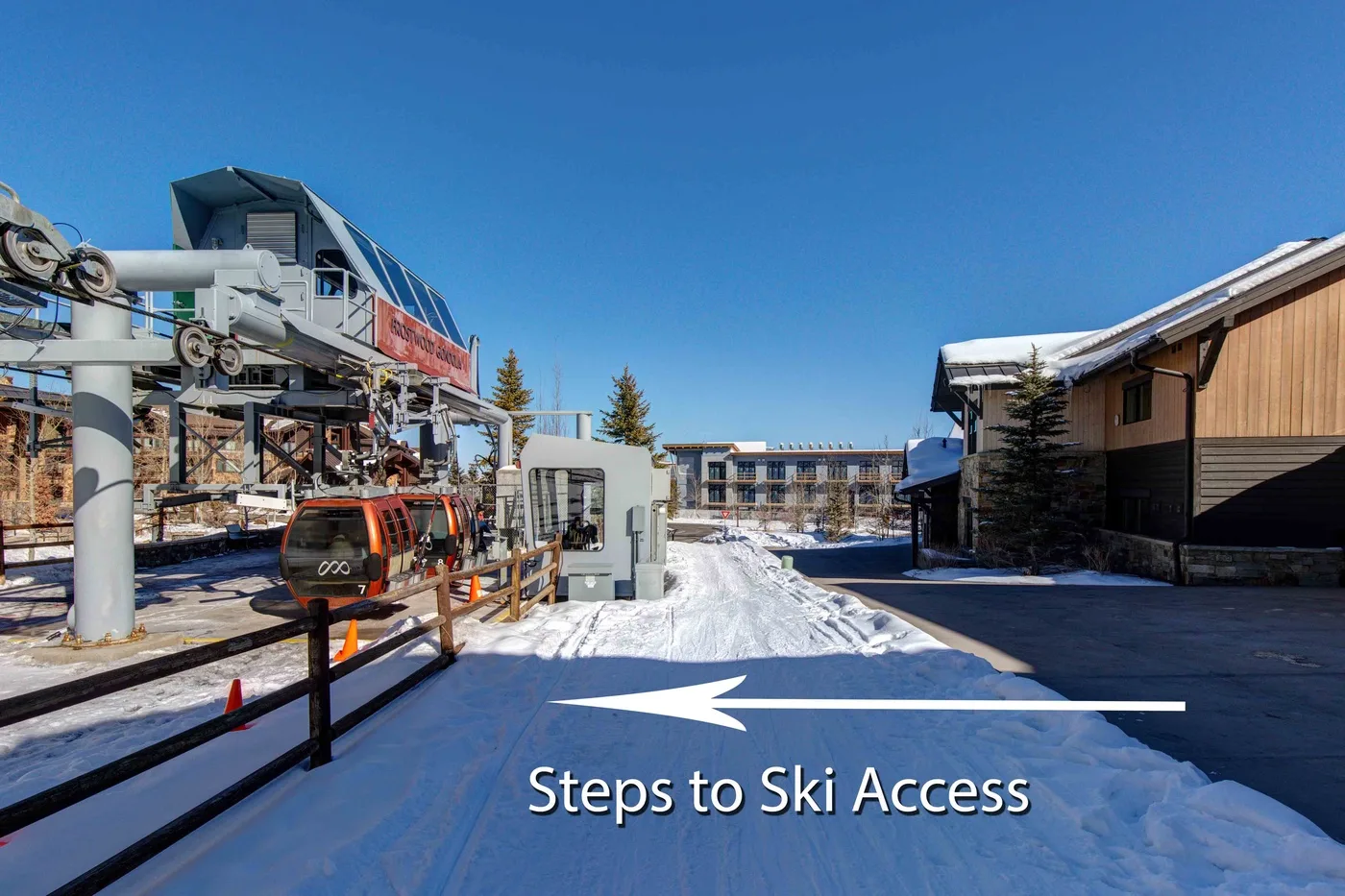 A snowy ski resort walkway leads toward a chairlift station between buildings.