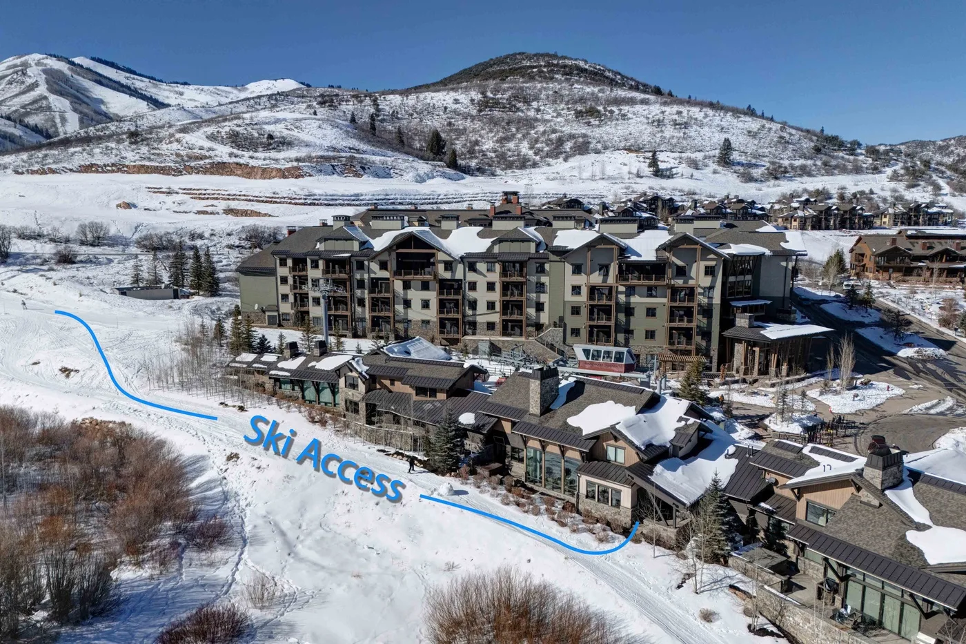 A mountain resort complex sits beside a snow-covered slope under a clear sky.