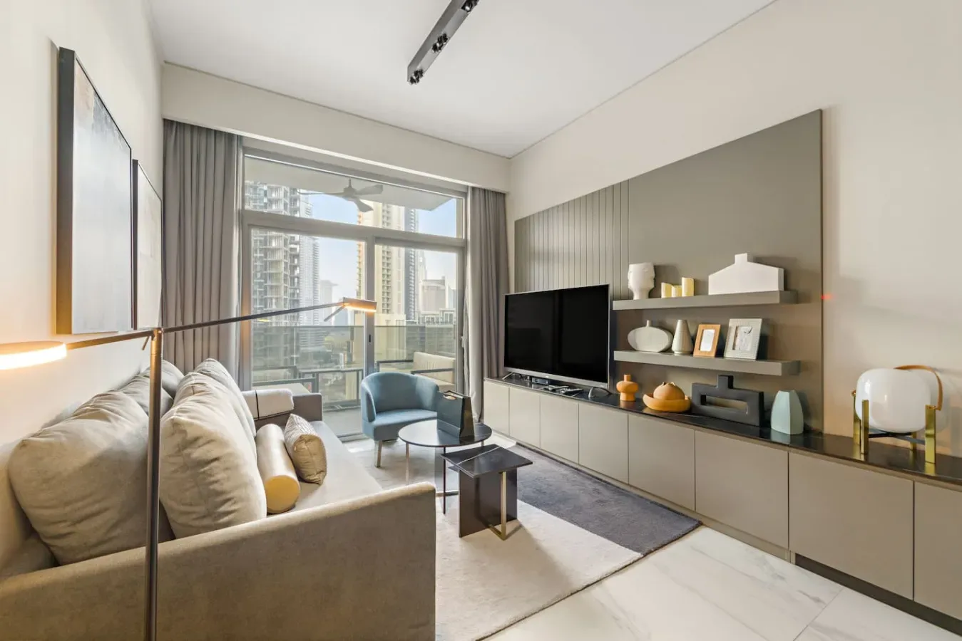 A bright living room with seating, a television, and large windows overlooking city buildings.
