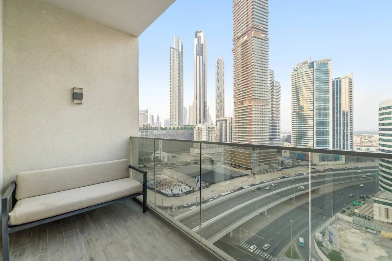 Un espacio de balcón con asientos da a un horizonte urbano y vías elevadas.