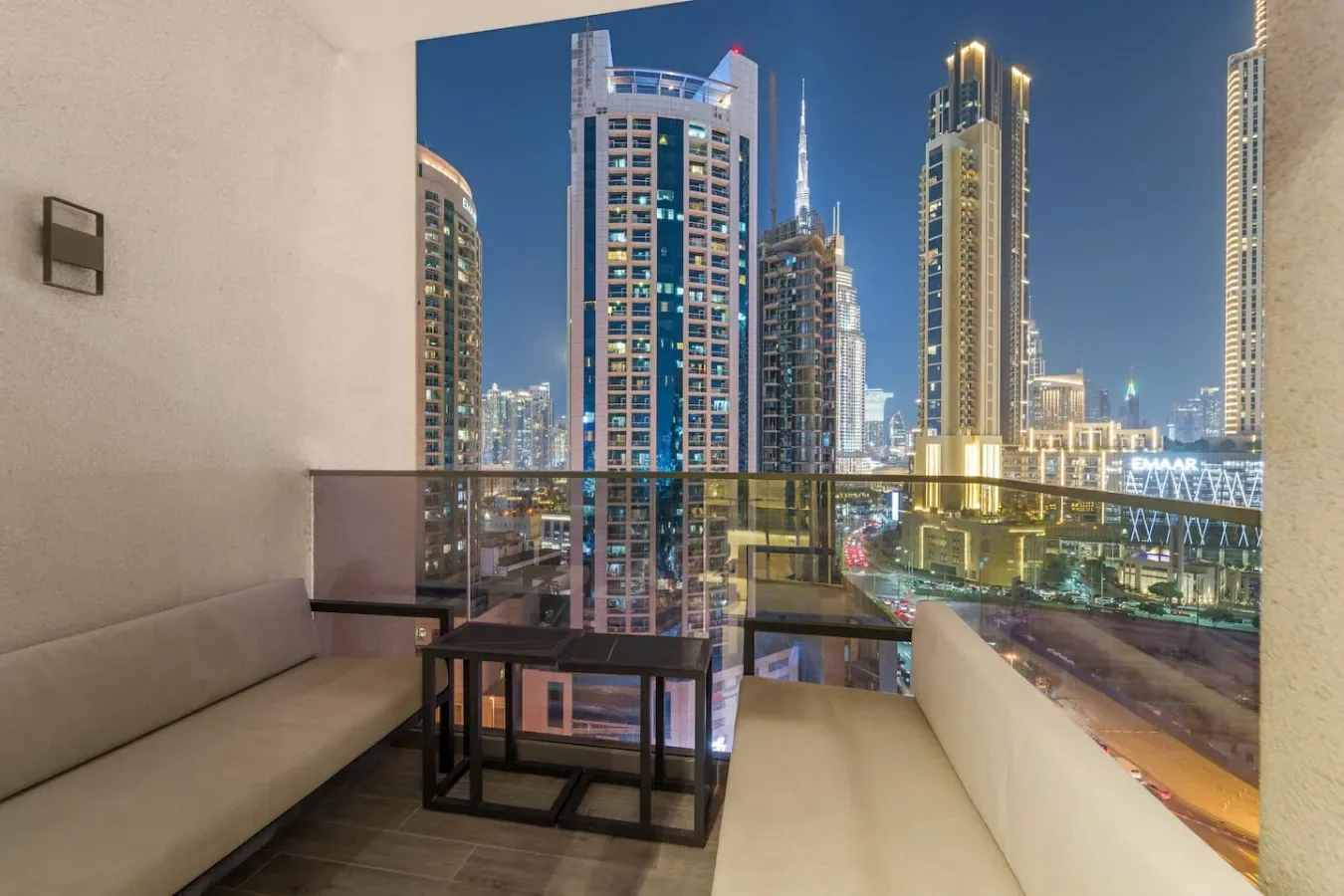 A balcony seating area overlooks illuminated high-rise buildings at night.
