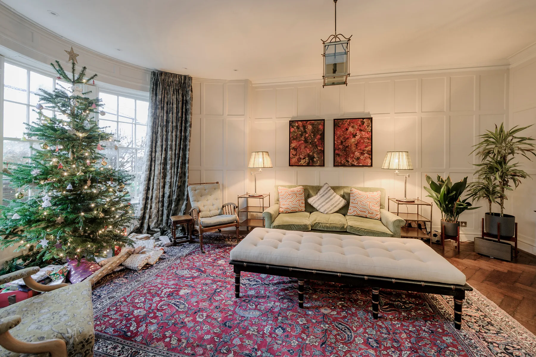 A living room with a decorated Christmas tree and seating around a large rug.