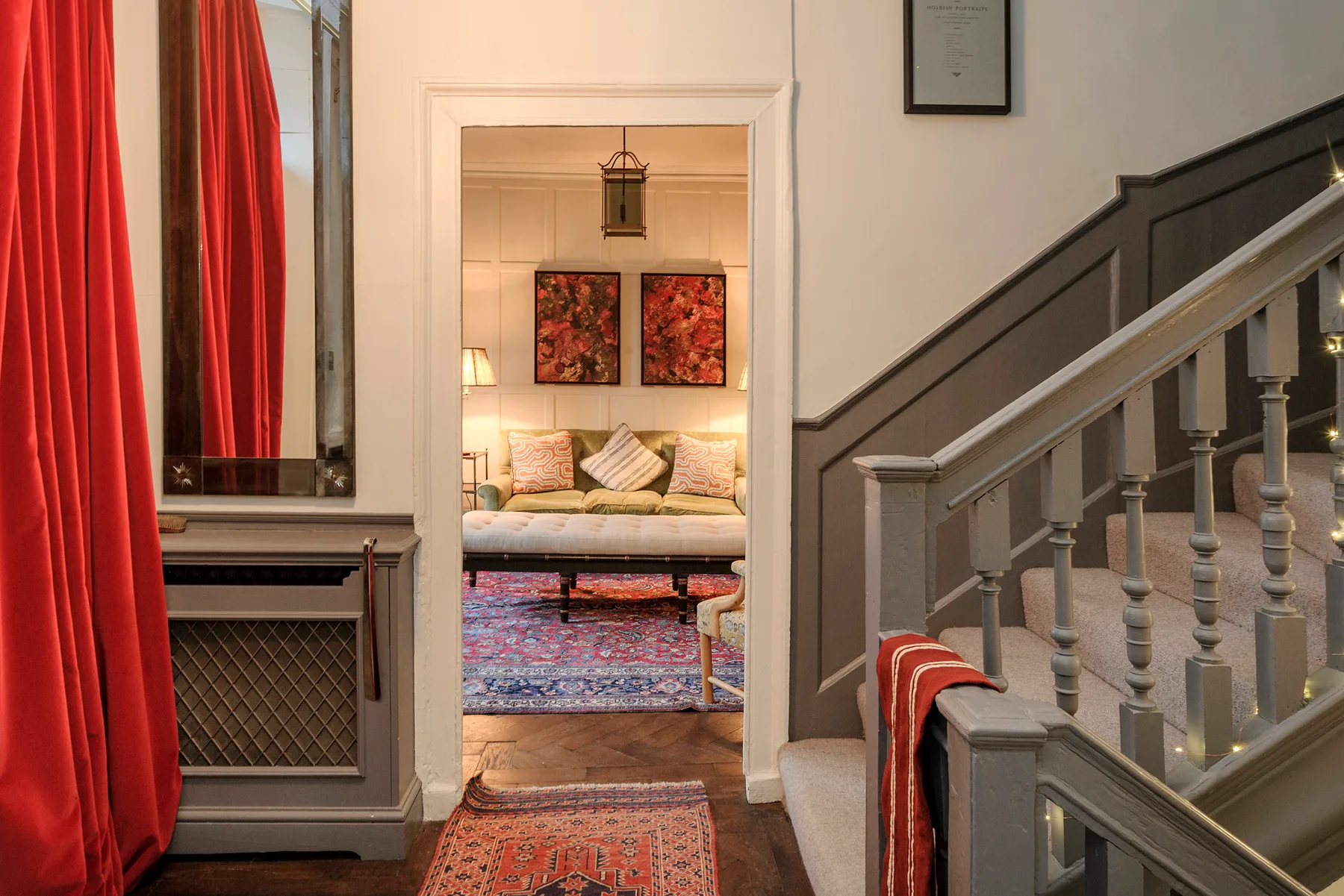 A living room with a sofa and colorful rug, seen through a doorway beside a staircase.