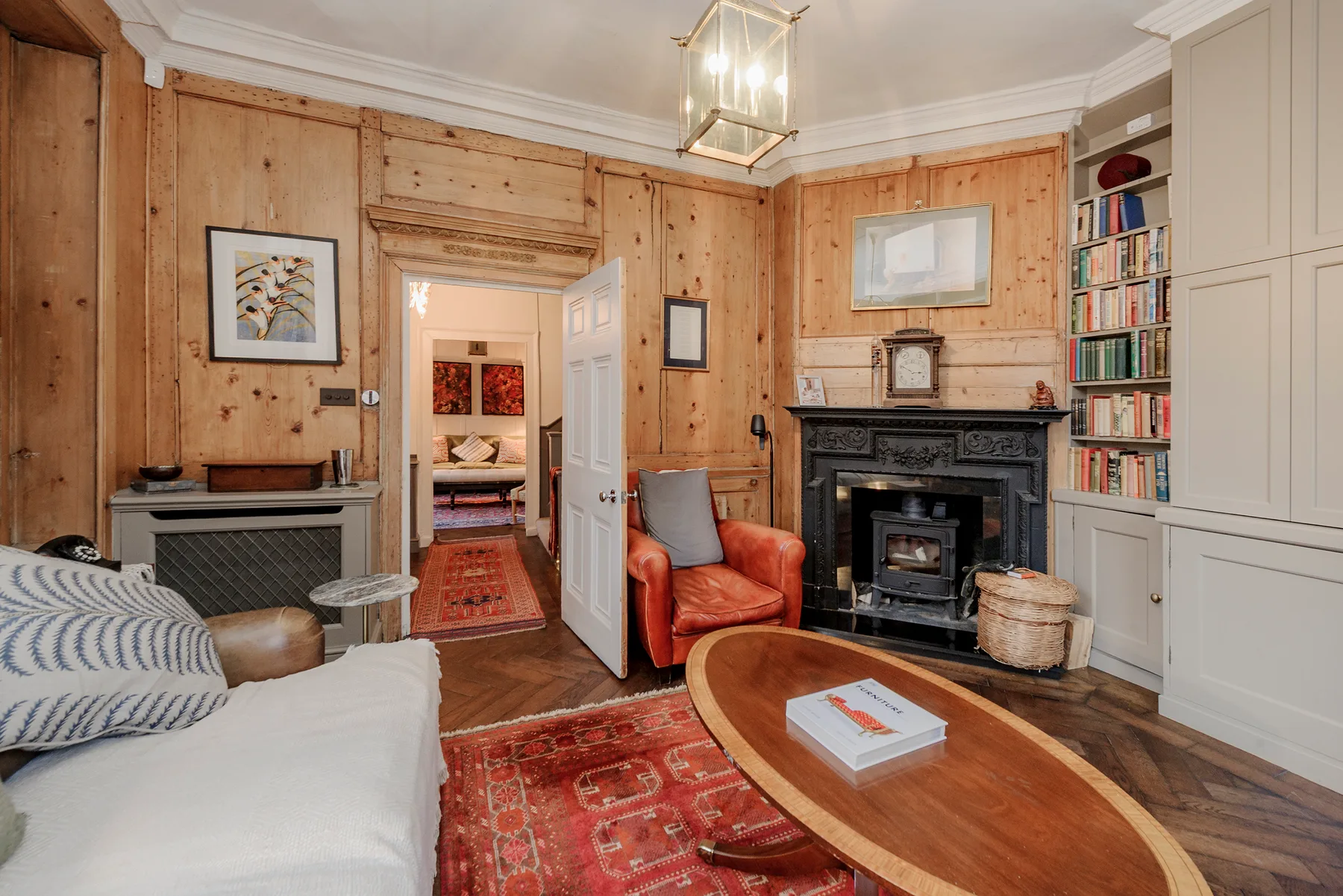 A wood-paneled living room with seating, a fireplace, and a red rug.