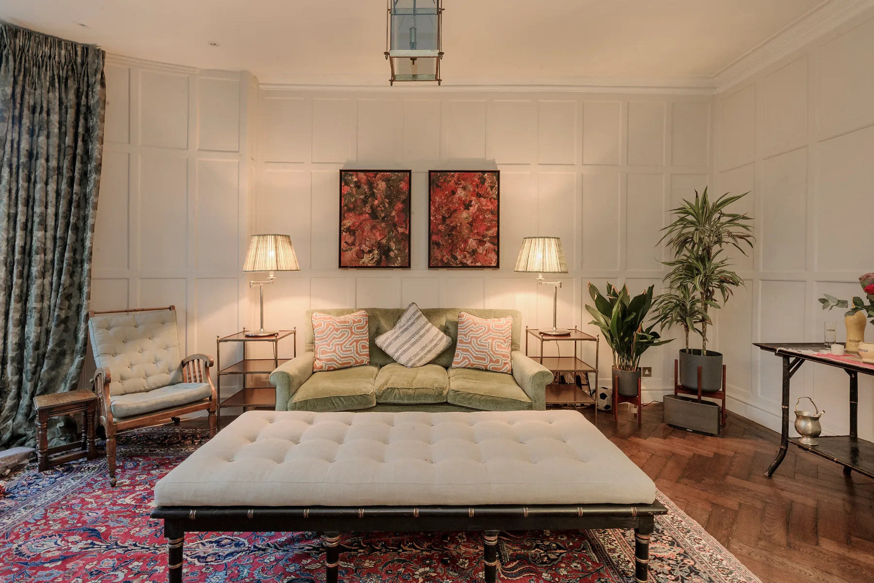 A living room with a green sofa, a tufted ottoman, and framed floral artwork.