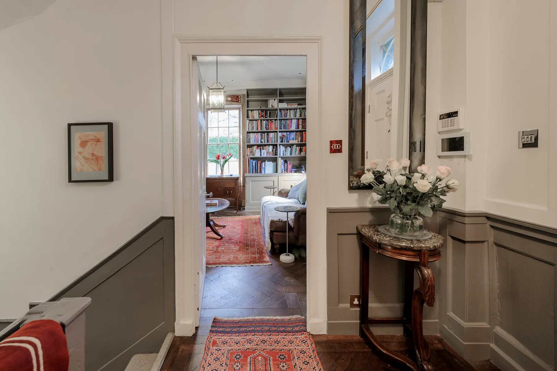 A paneled hallway opens into a bright sitting room with bookshelves and a rug.