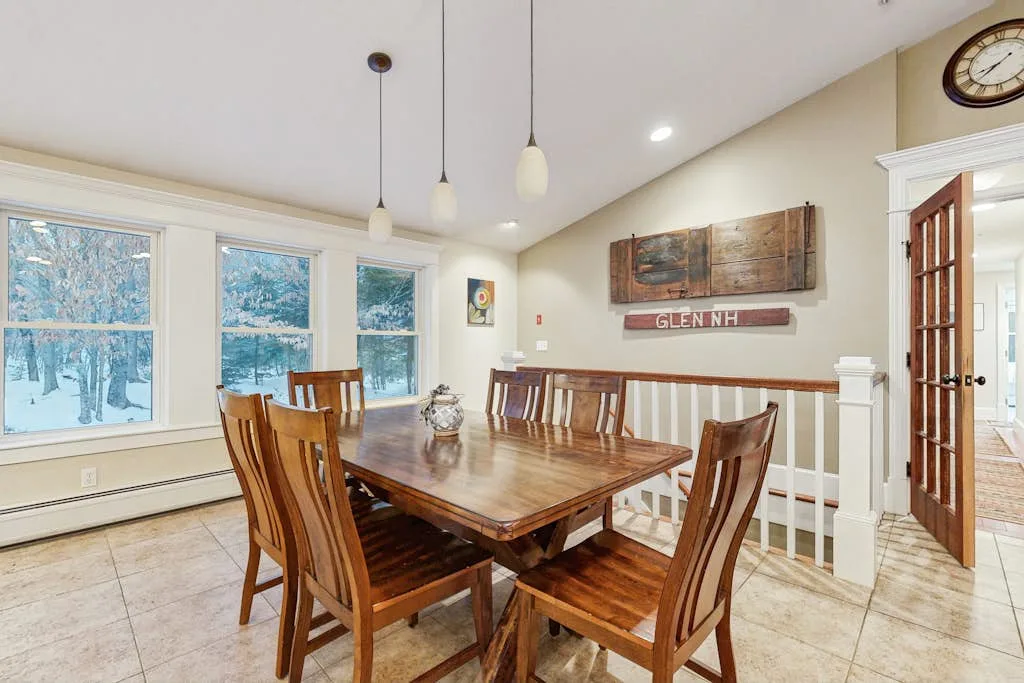 Un comedor con una mesa de madera y sillas junto a grandes ventanas.