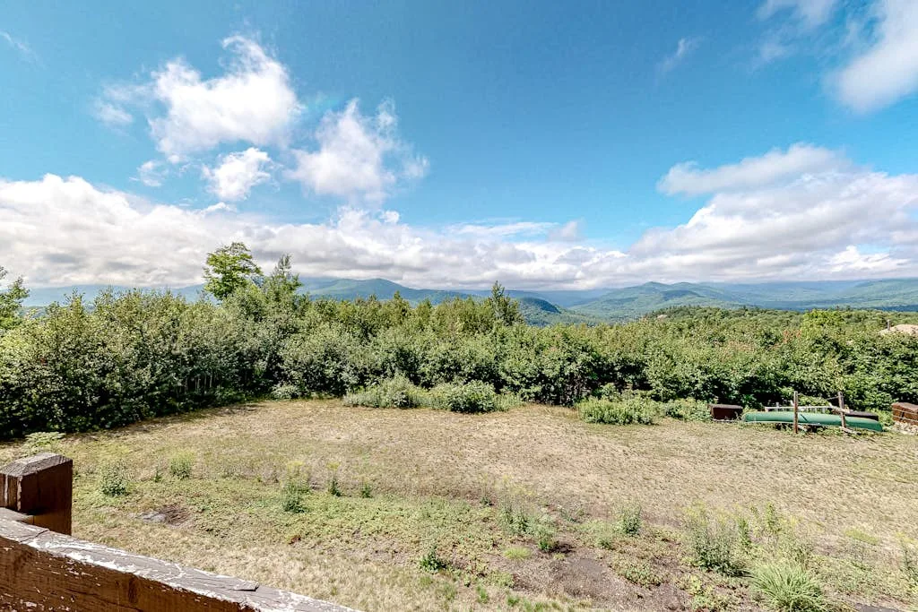 Un claro abierto de hierba está rodeado de arbustos, con colinas lejanas bajo un cielo azul.