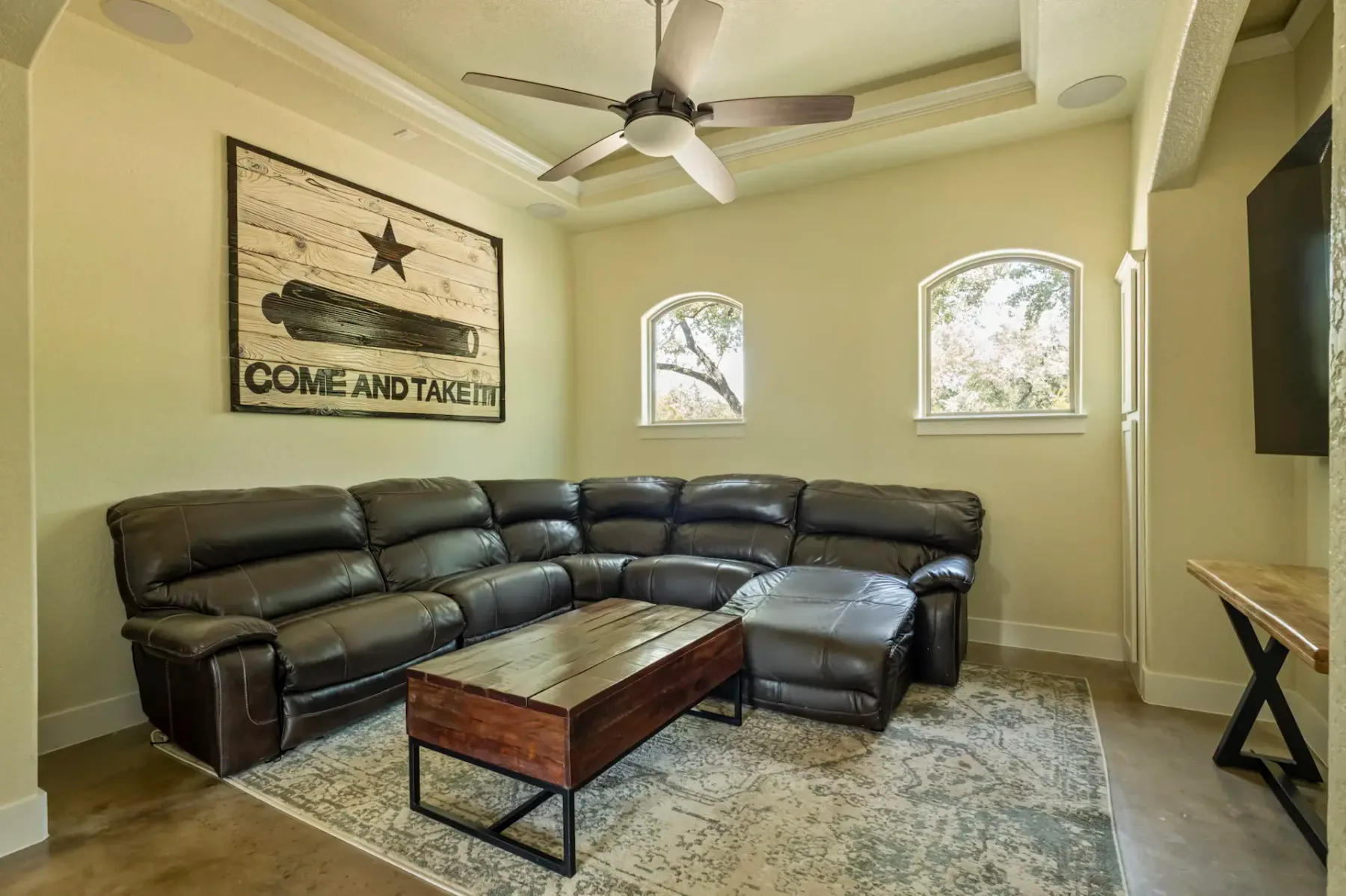 A cozy living room with a black leather sectional sofa, wooden coffee table, ceiling fan, and a