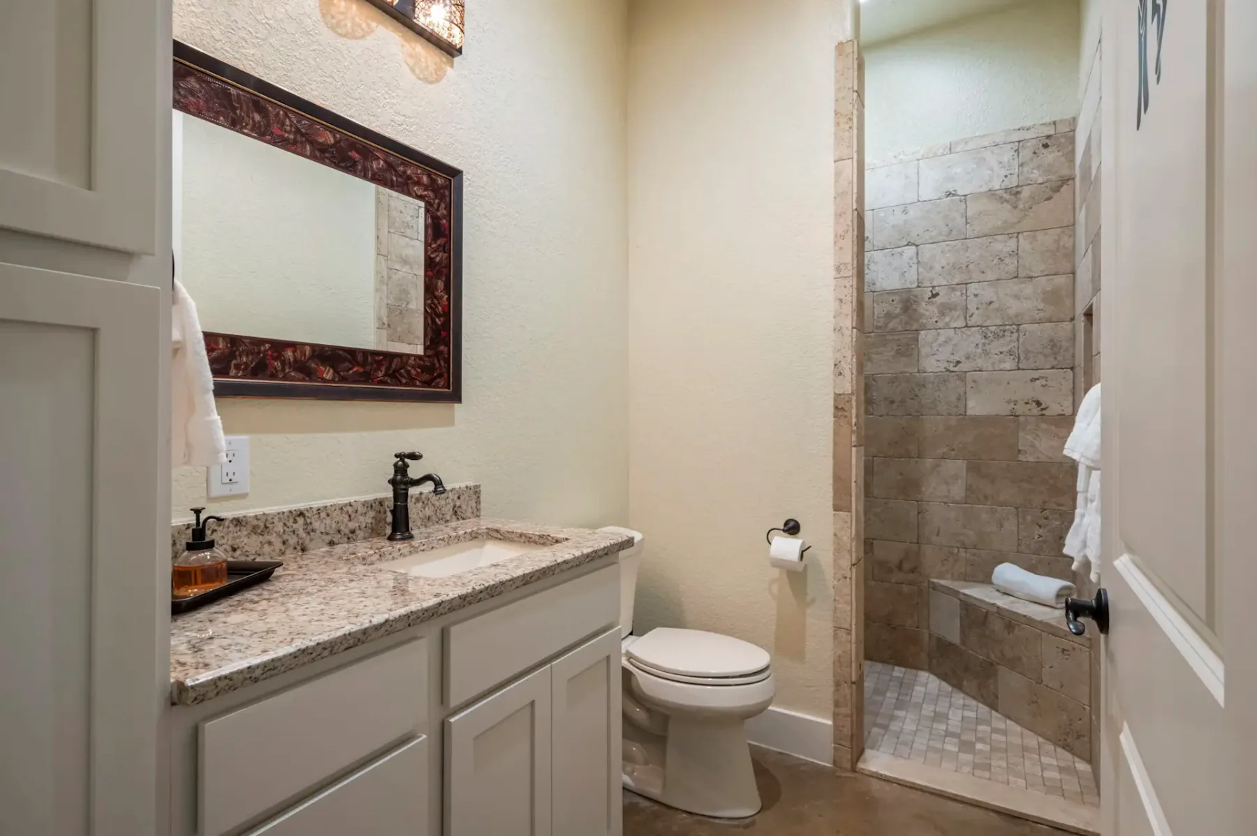 Bathroom with granite countertop, white cabinets, wall mirror, toilet, and a tiled walk-in shower with a glass door.