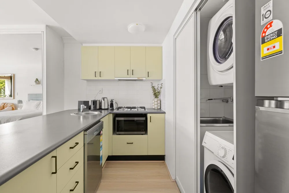 Cocina compacta con gabinetes claros y una lavadora visible al lado.