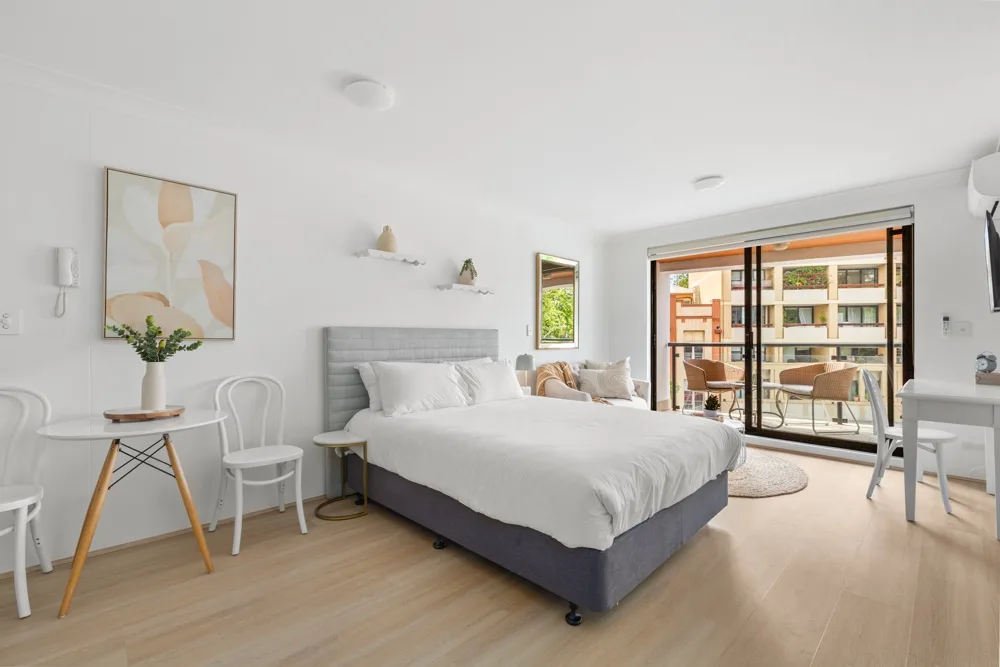 Dormitorio luminoso con una cama y puertas de vidrio que dan a un balcón.