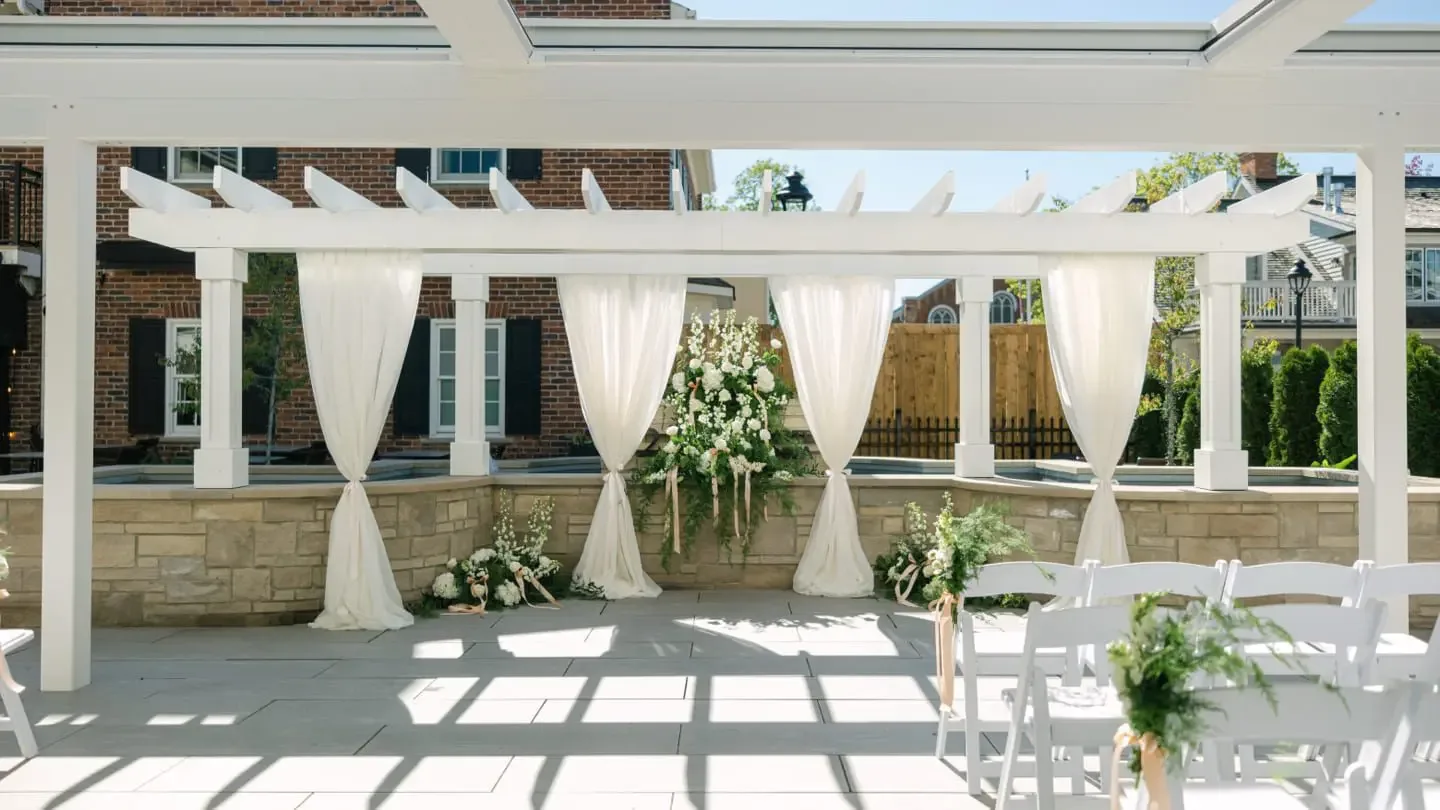 Outdoor wedding setup beneath a white pergola.