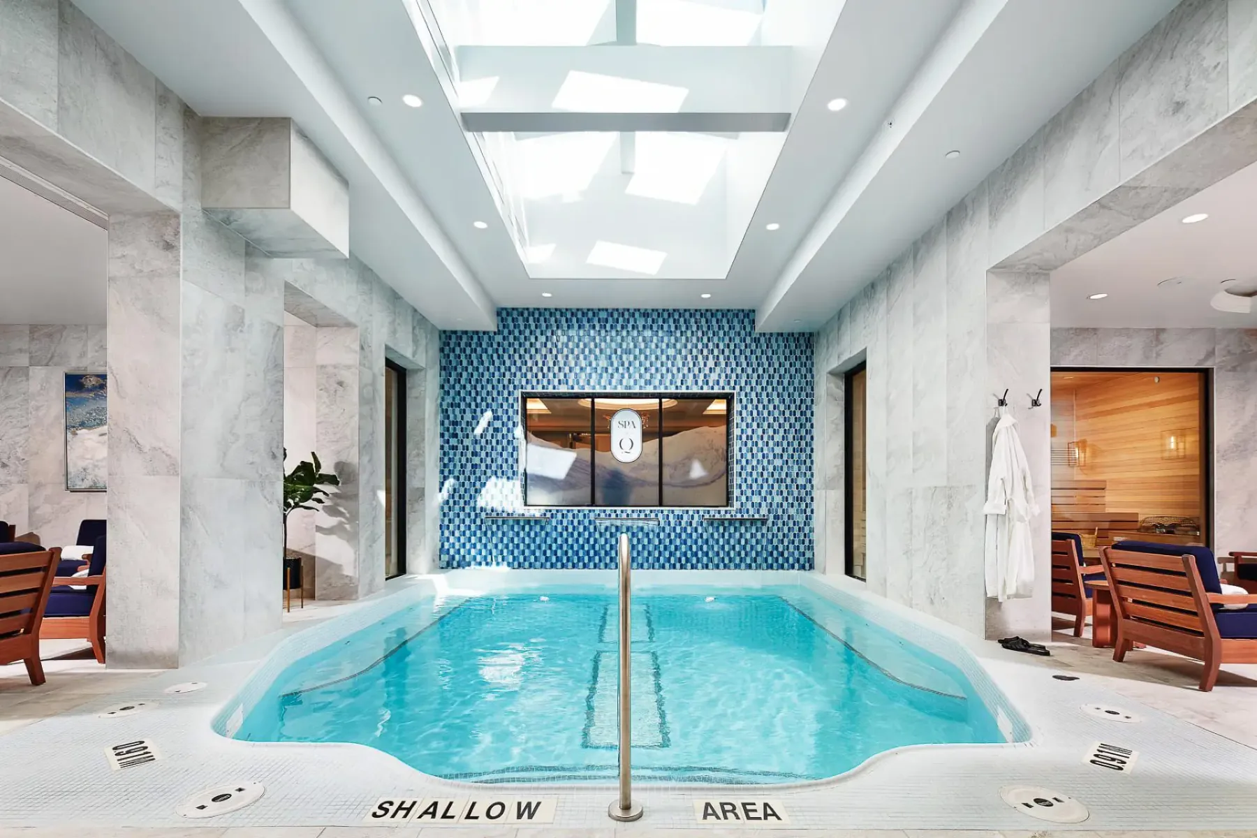 Indoor spa pool beneath a skylight, with lounge chairs and a sauna visible.