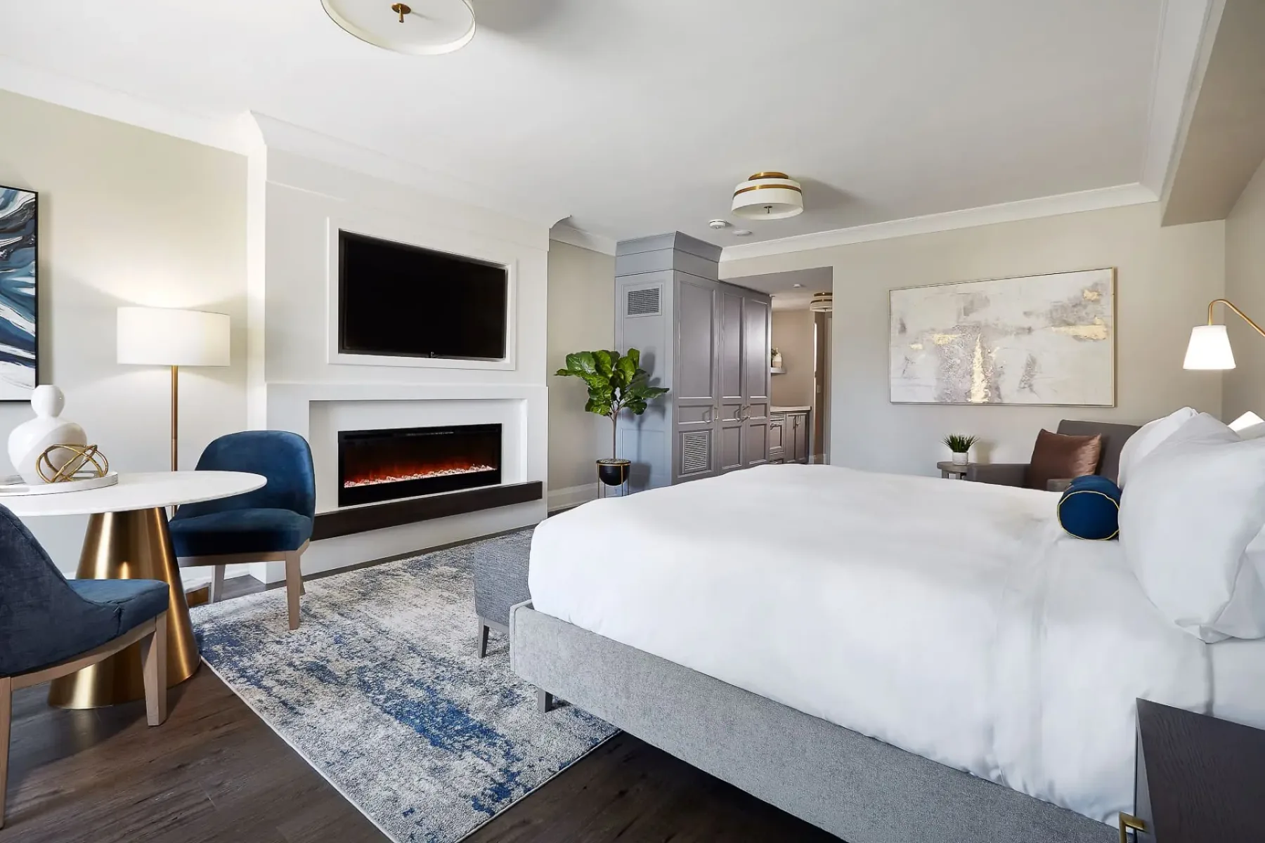 Hotel room with a king bed, sitting area and electric fireplace.