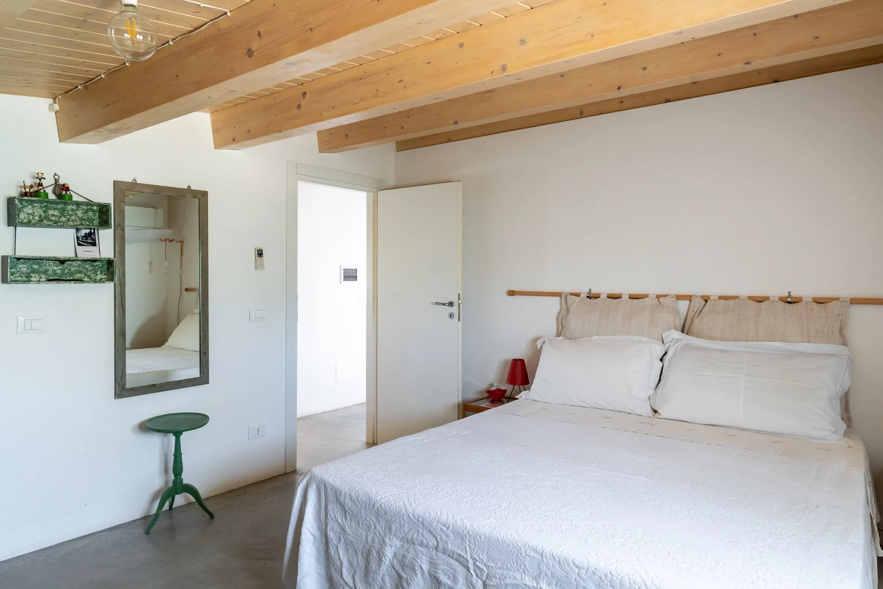 Un dormitorio luminoso con una cama grande bajo vigas de madera expuestas en el techo.