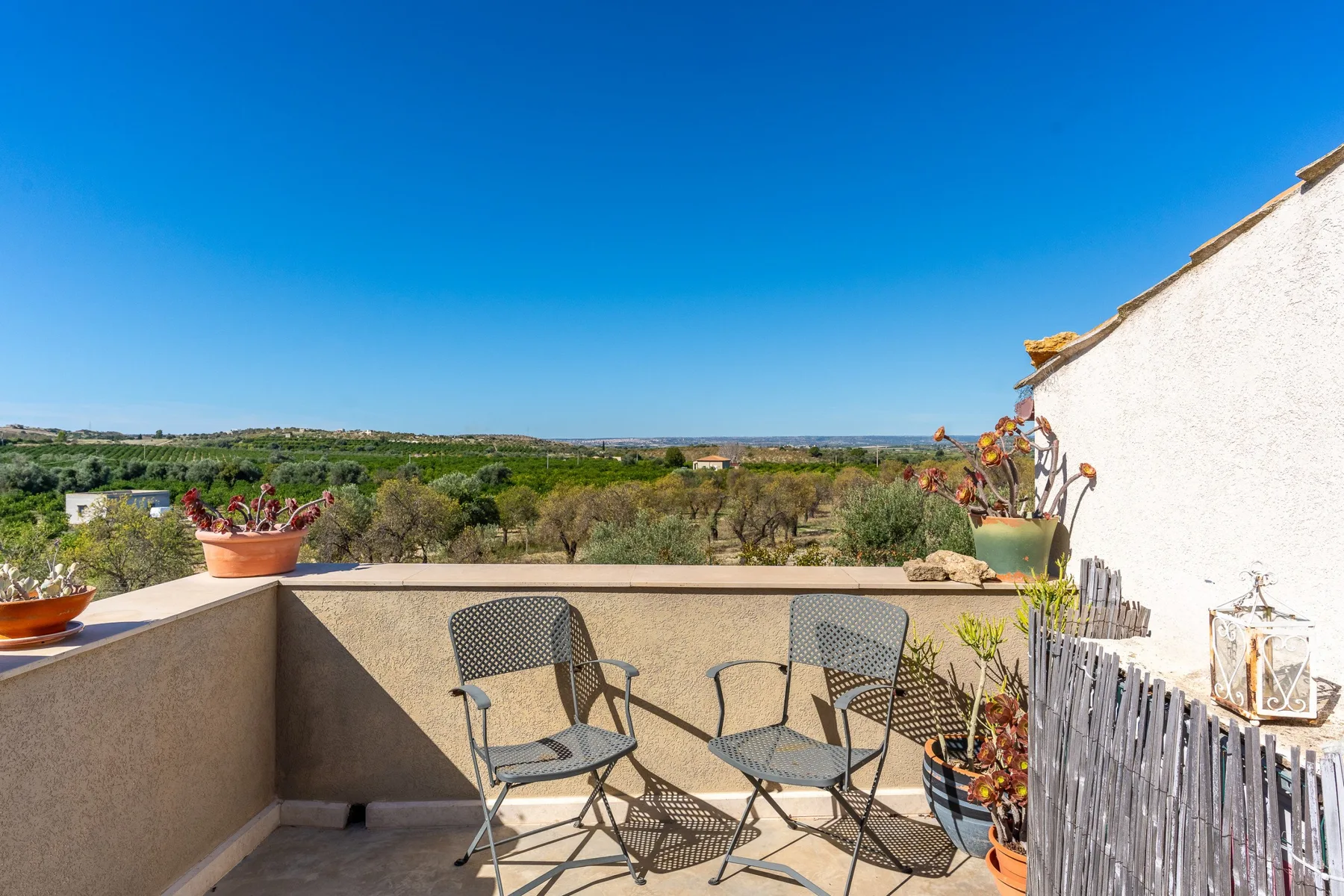 Una terraza soleada tiene dos sillas junto a un muro bajo, con vistas al campo verde.