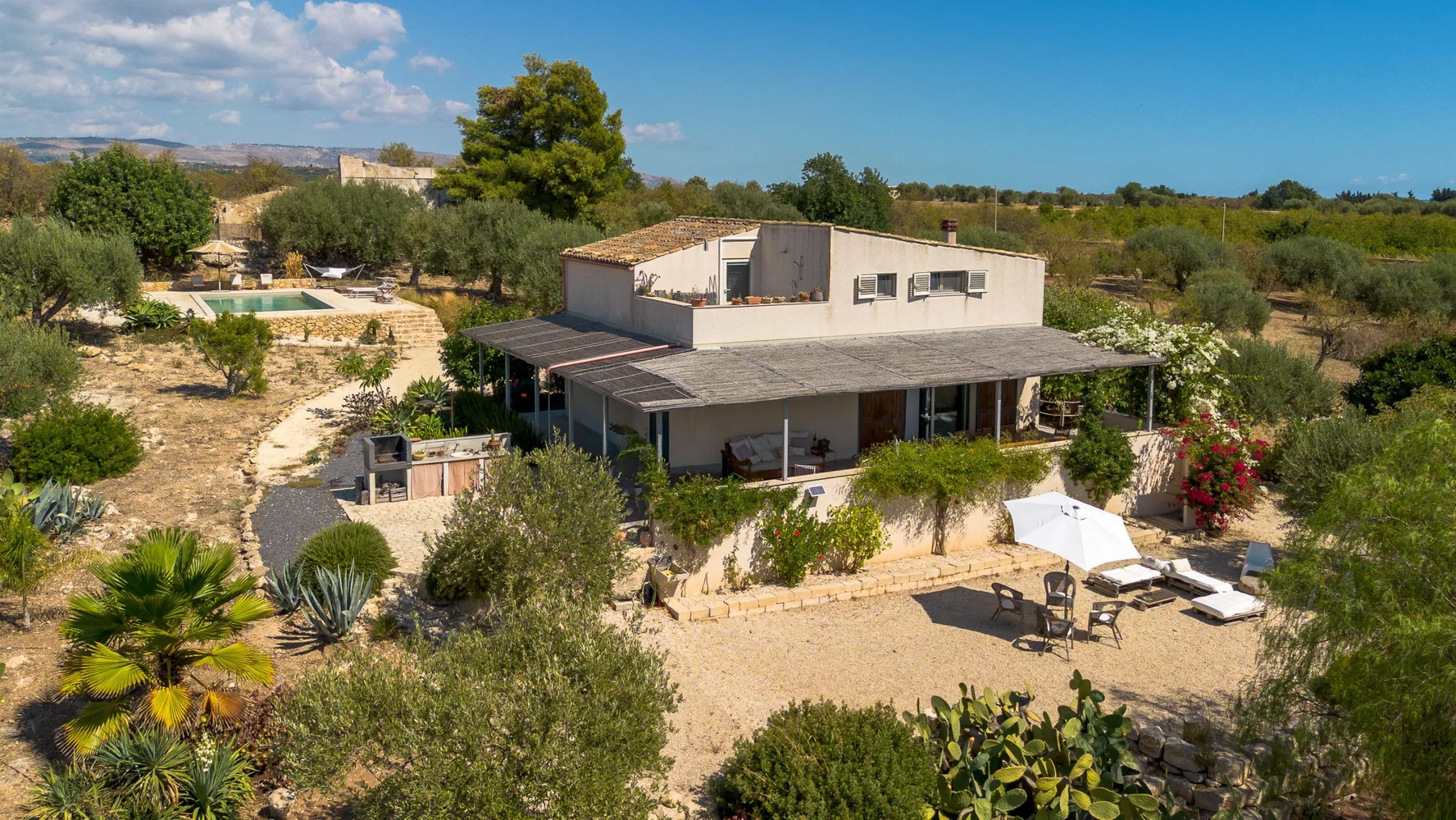 Una casa moderna está rodeada de jardines, con una piscina y asientos al aire libre.