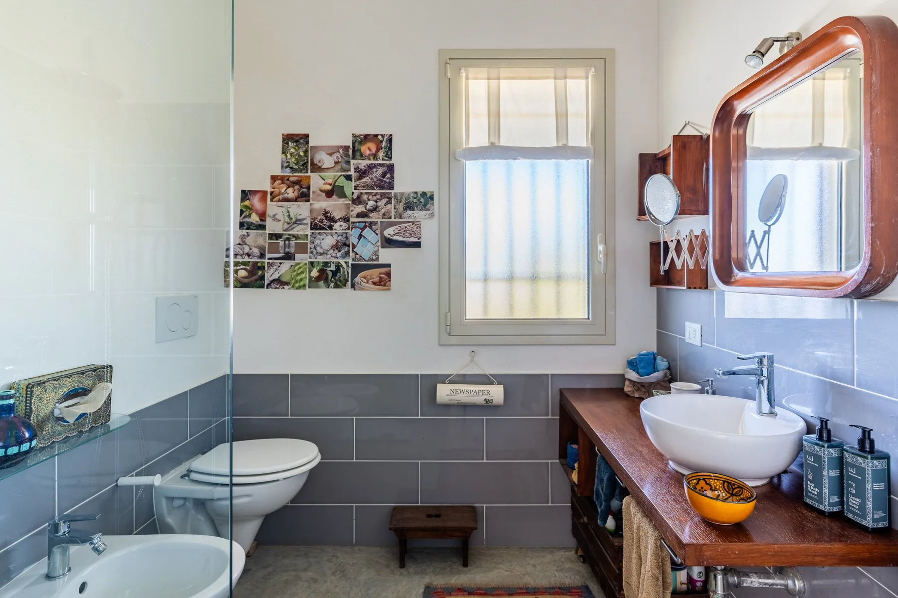 Un baño con ducha, inodoro y lavabo bajo una ventana.