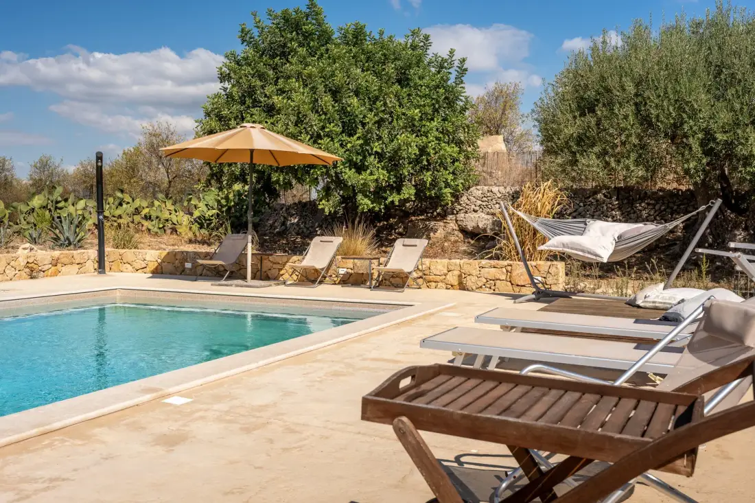 Una piscina al aire libre junto a un patio pavimentado con tumbonas y una hamaca.