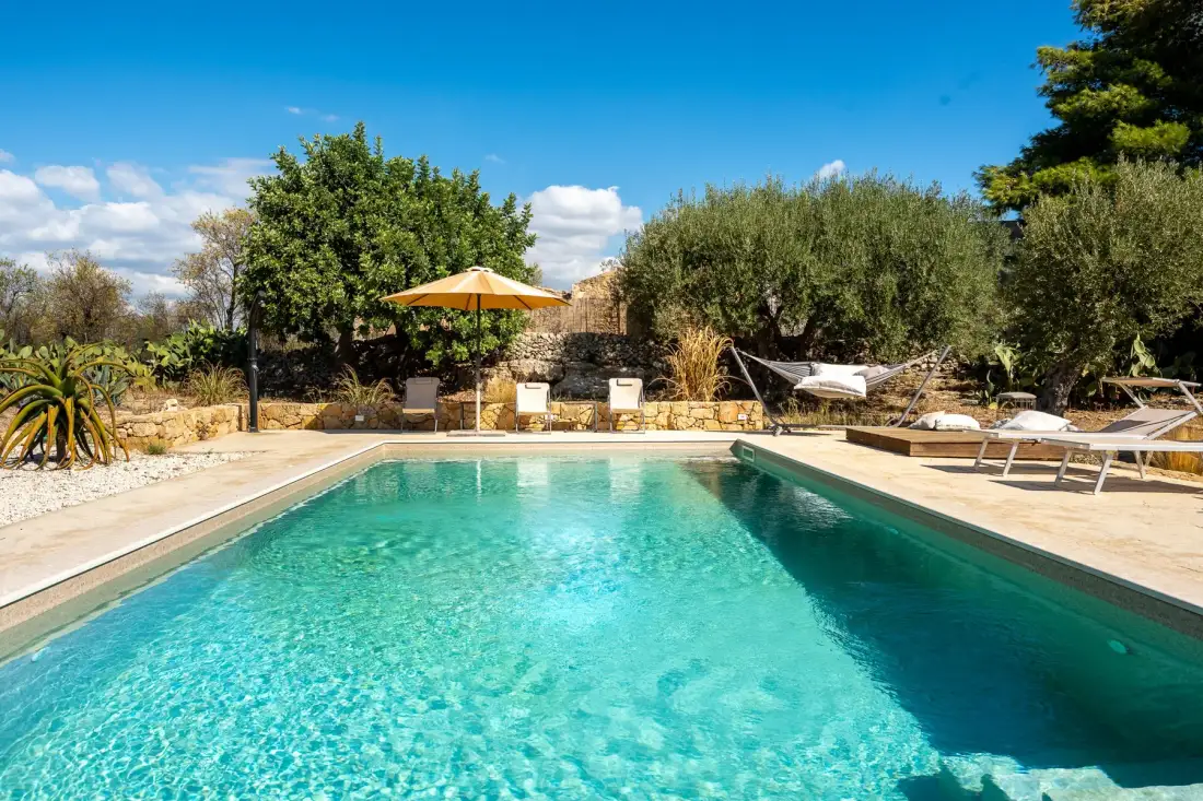 Una piscina al aire libre junto a una terraza de piedra y árboles.
