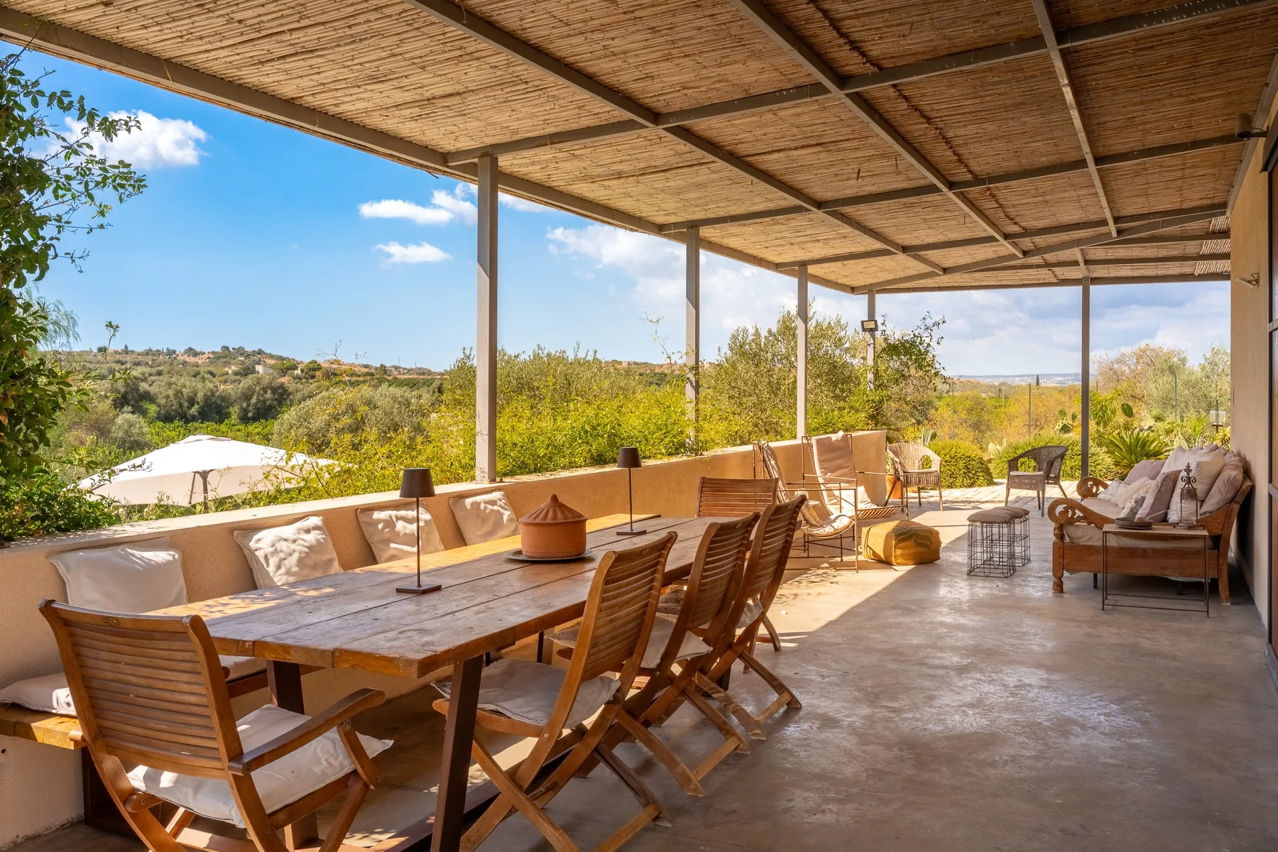 Una terraza exterior cubierta con una mesa larga que da a un paisaje verde.