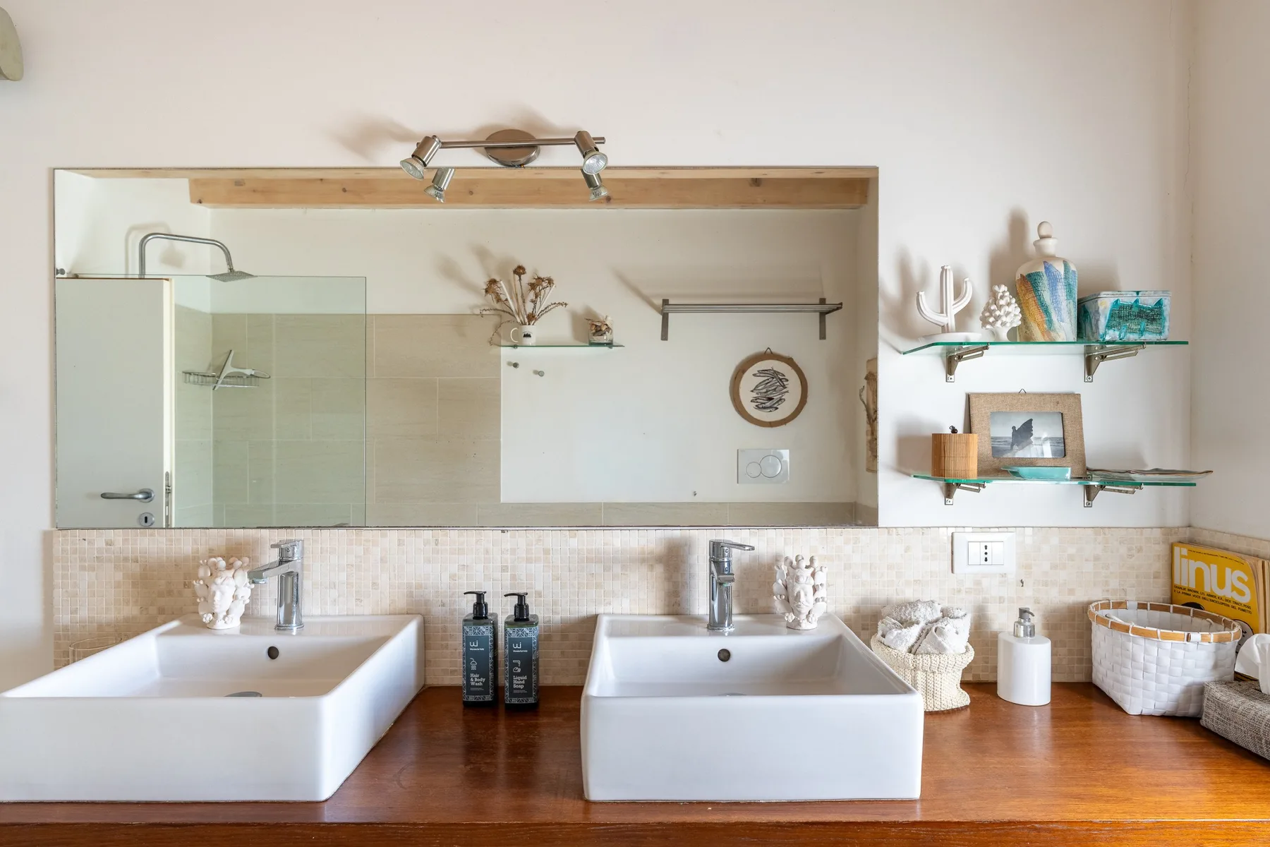 Un tocador de baño con dos lavabos, un espejo amplio y estantes abiertos.