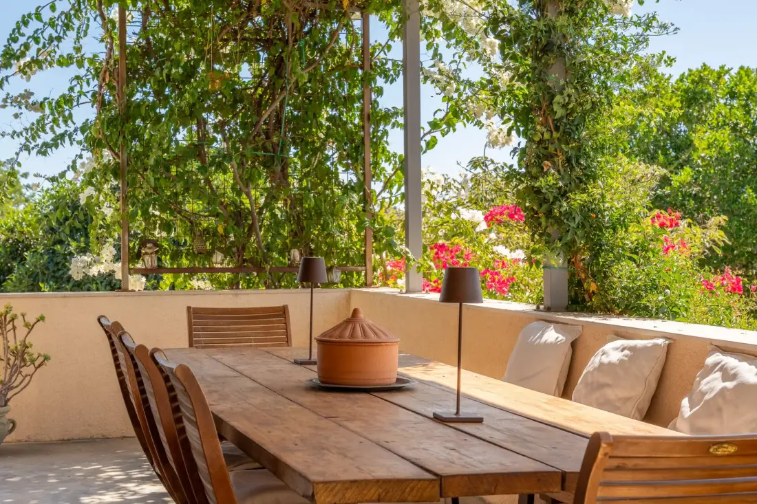 Un comedor al aire libre con una mesa larga de madera y vegetación frondosa.