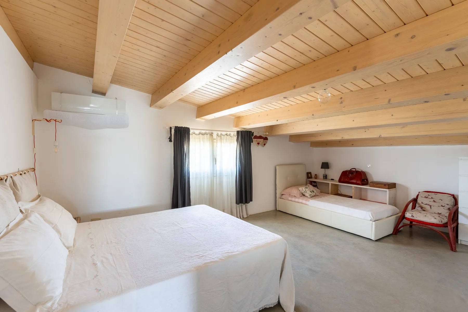 Un dormitorio con camas y una ventana bajo un techo inclinado de madera.