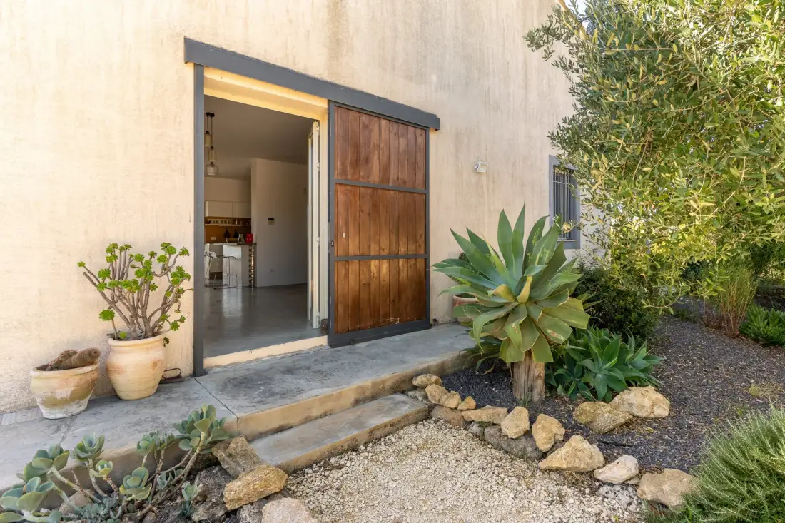 Una entrada de madera abierta da a un interior luminoso, con plantas junto a la puerta.