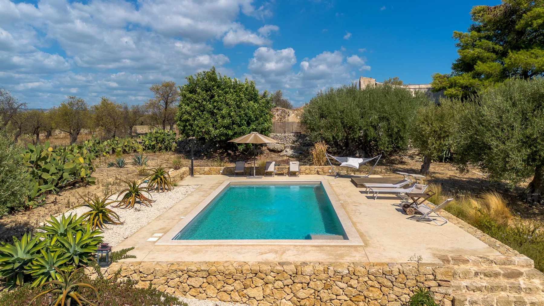 Una piscina al aire libre está rodeada de árboles y jardines.