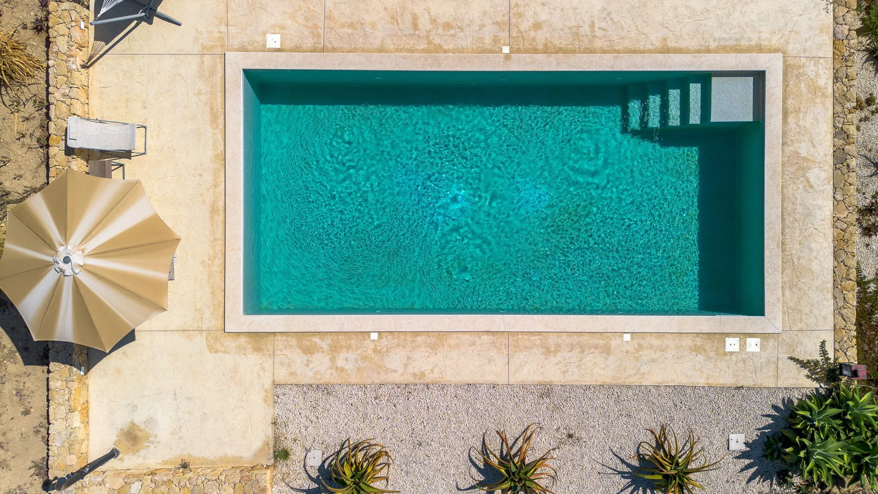 Vista desde arriba de una piscina rodeada por un patio pavimentado.