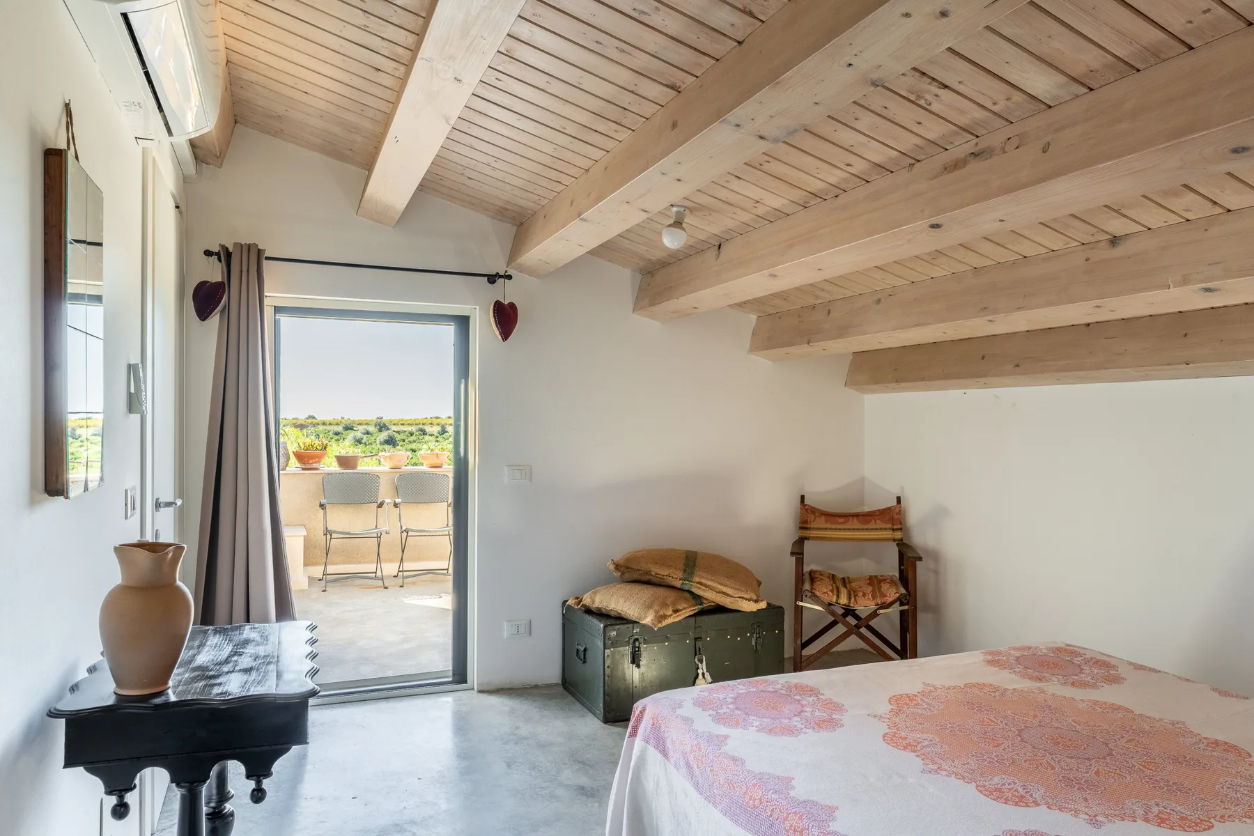 Un dormitorio con una cama, un arcón y una puerta abierta a un balcón.