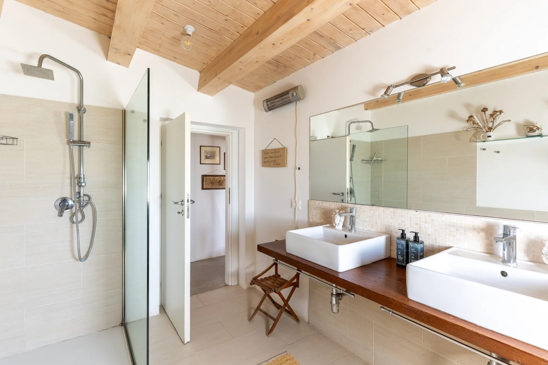 Un baño con una ducha de vidrio y un tocador largo con dos lavabos.