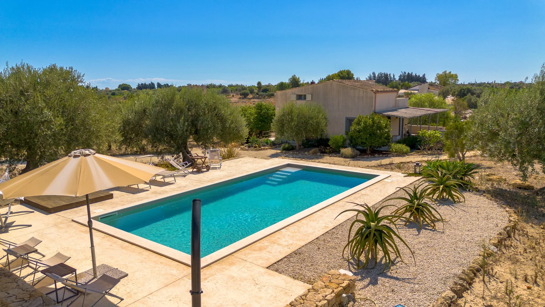 Una piscina al aire libre con una terraza pavimentada y vegetación alrededor.