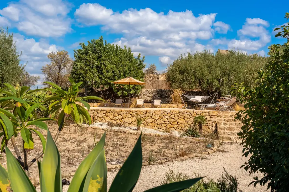 Una terraza de piedra con asientos al aire libre y una sombrilla abierta entre árboles.