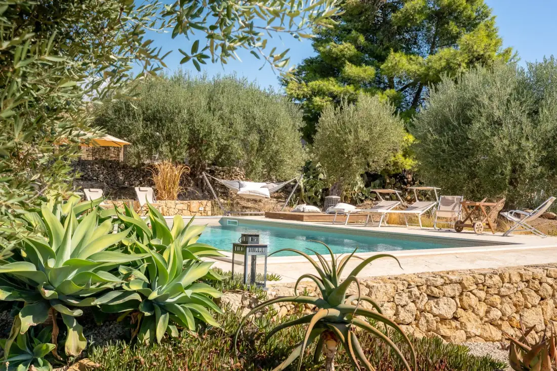 Una piscina al aire libre rodeada de vegetación y asientos de descanso.