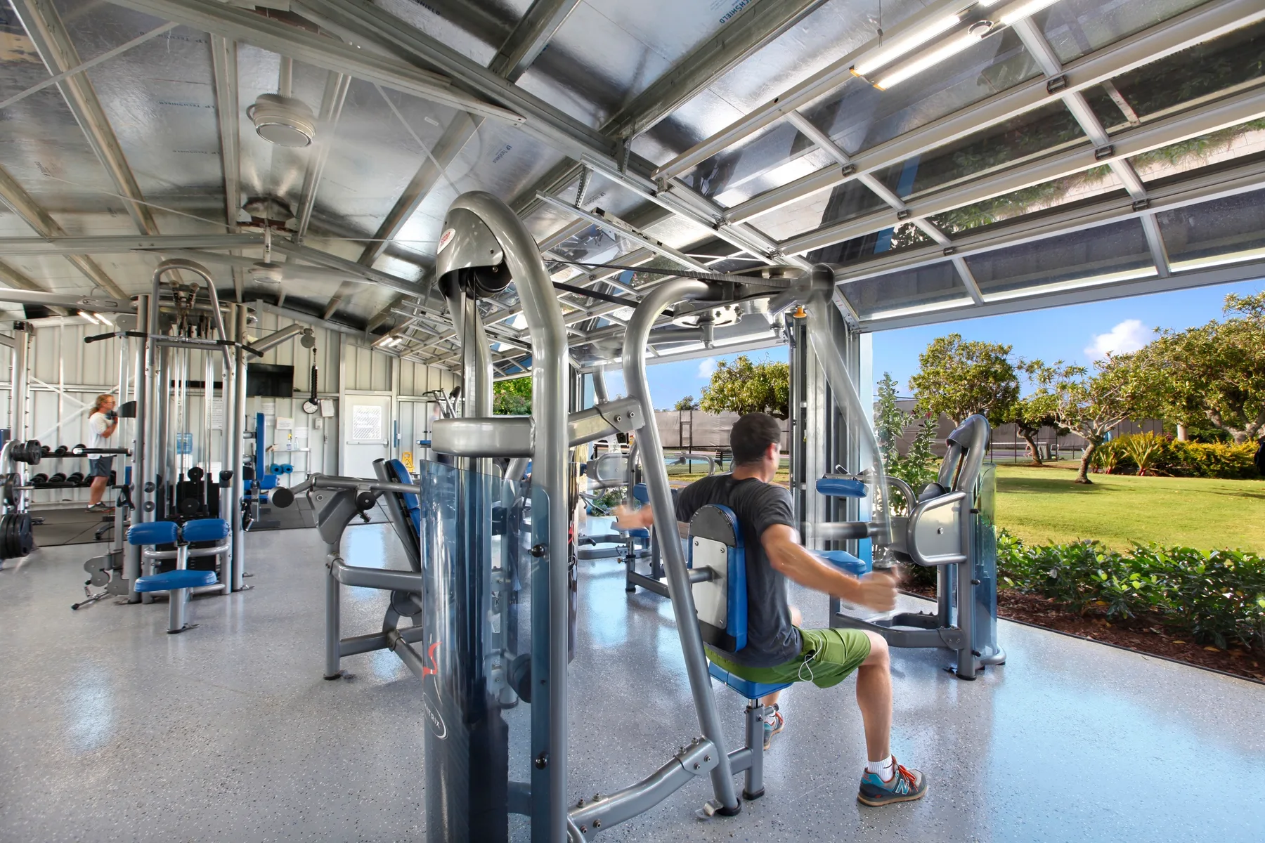 Un gimnasio con máquinas de ejercicio y grandes ventanales con vistas a una zona verde.
