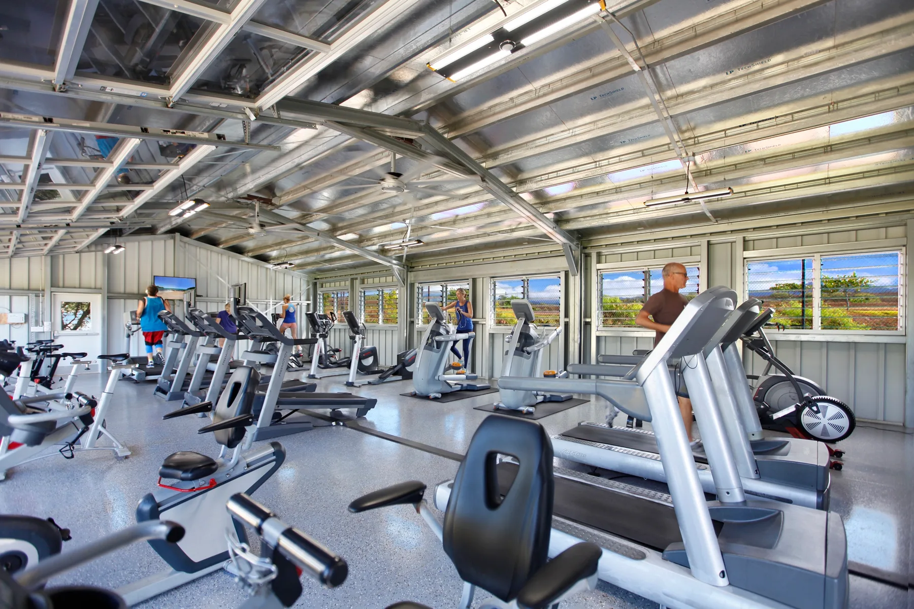 Un gimnasio con máquinas de ejercicio y ventanas amplias.