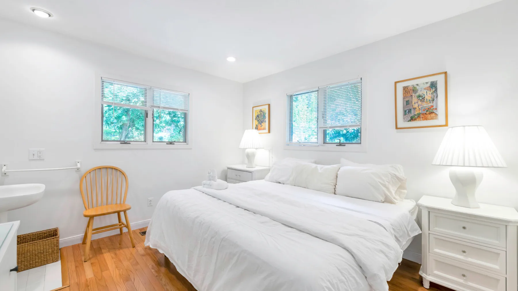 Un dormitorio luminoso con una cama blanca, mesitas de noche y ventanas.
